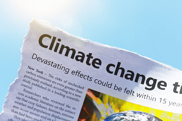 photo of a newspaper article warning of worsening climate change as the planet warms, shown outside against a blue sky and sun